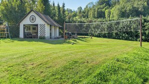 Une maison de campagne avec une grande fenêtre ronde, un filet de volley-ball et une cour couverte d’herbe.