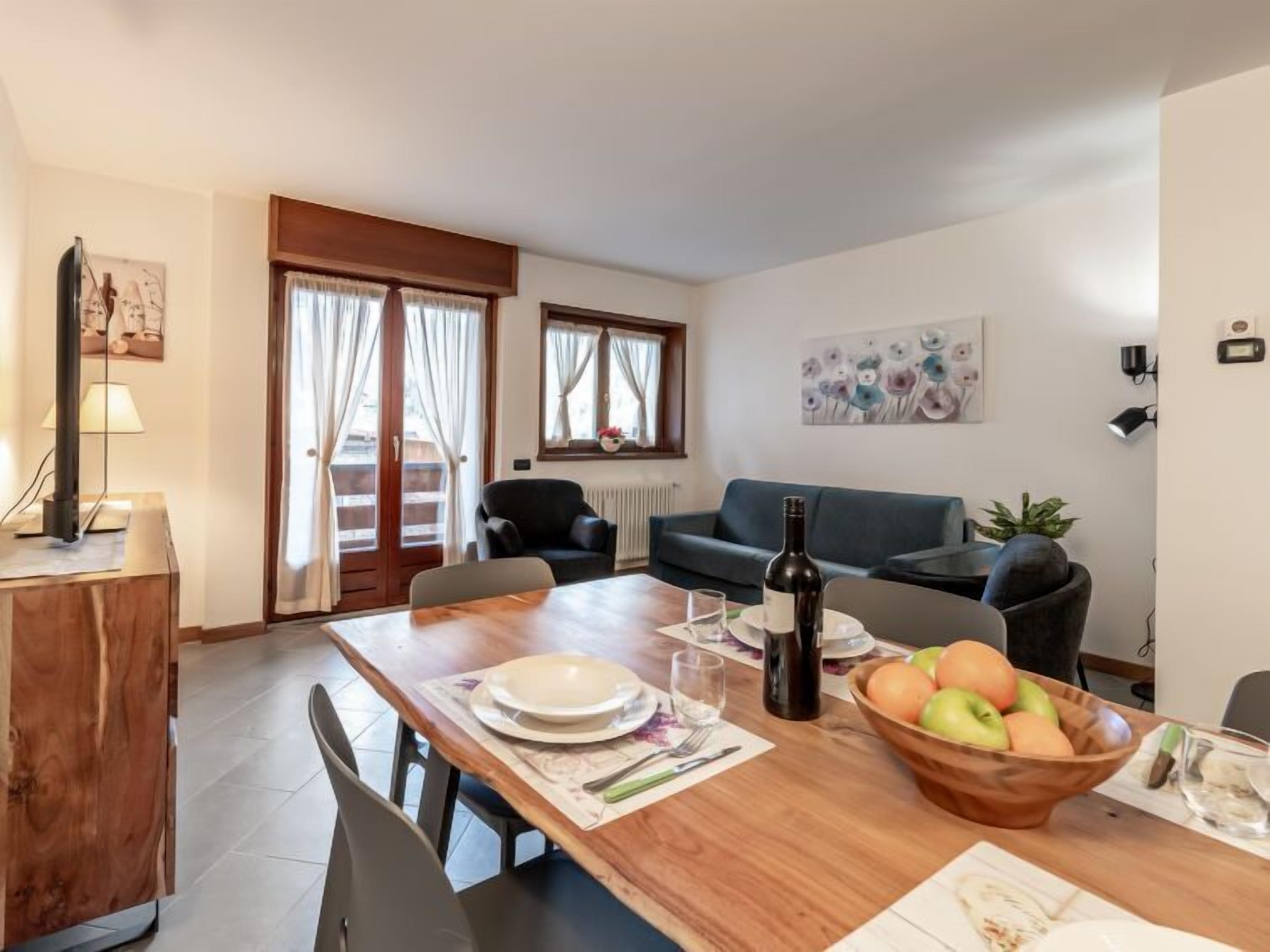 Een eetgedeelte met een houten tafel gedekt voor twee personen, een fruitschaal en een fles wijn.