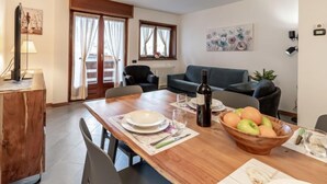 A dining area with a wooden table set for two, a bowl of fruit, and a bottle of wine. - Condominio Giulia by Interhome (Canazei)
