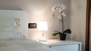 A neatly made bed with white bedding, a bedside lamp, a potted orchid, and a small bedside table with drawers. - Condominio Giulia by Interhome (Canazei)