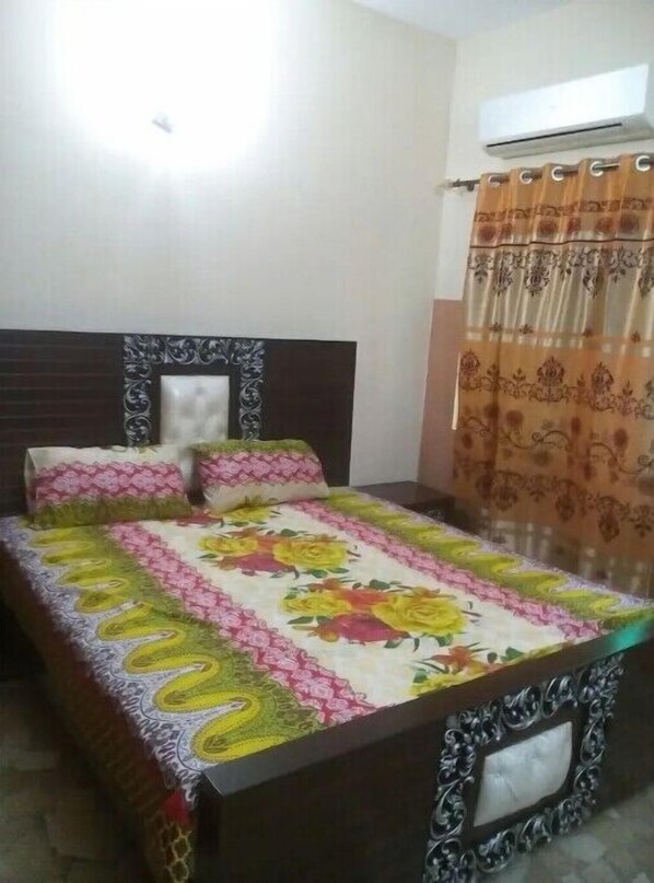 A bed with a floral bedspread, a dark wooden headboard, and a curtain with a floral pattern.