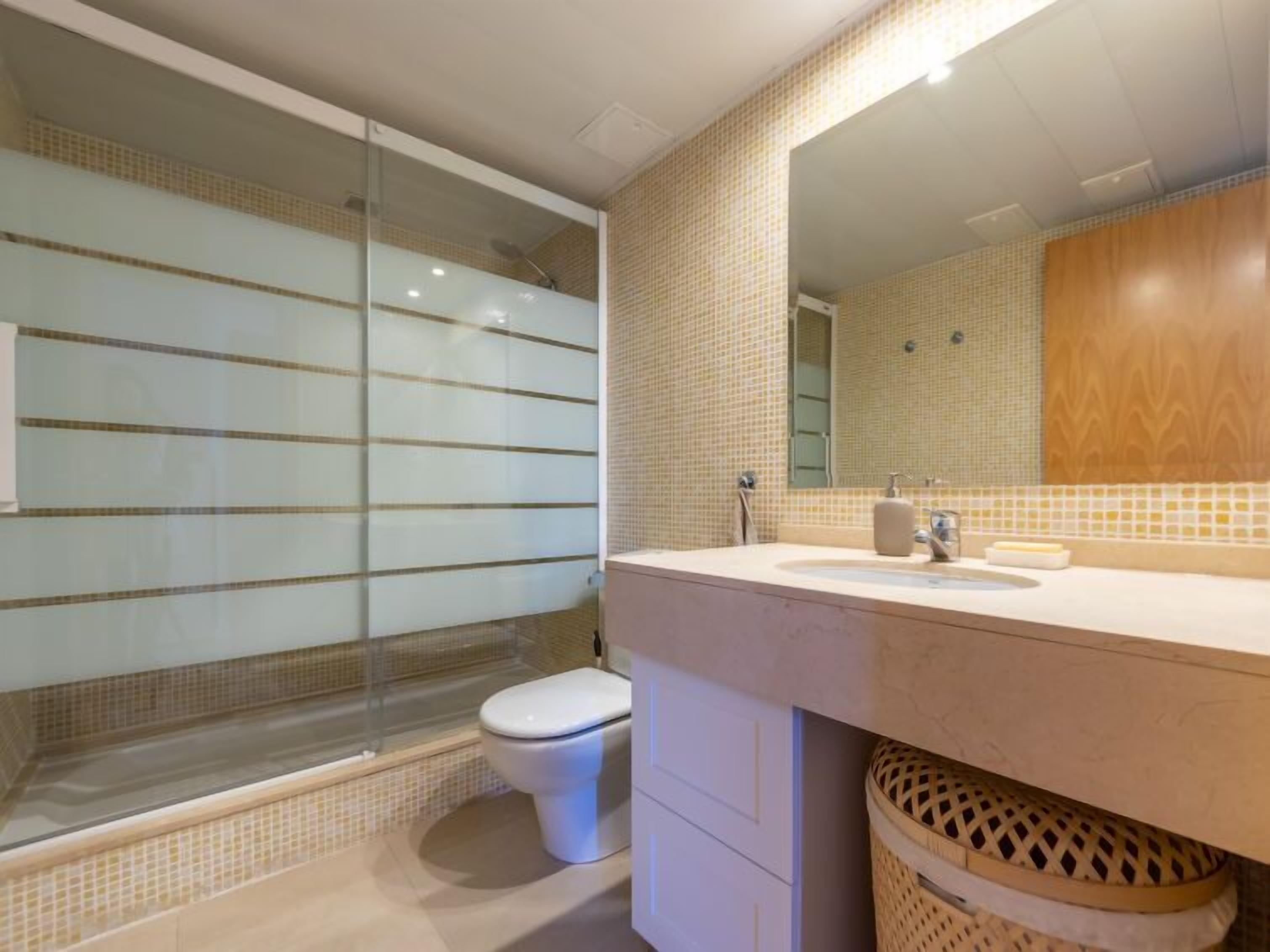 Ein modernes Badezimmer mit Duschkabine aus Glas, einer weißen Toilette und einem beigefarbenen Waschtisch mit Spiegel.