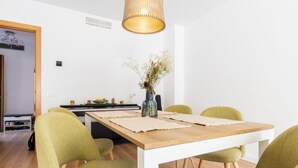 Ein Essbereich mit einem Holztisch, vier grünen Stühlen, einer Hängelampe und einem Blumenstrauß auf dem Tisch.