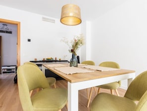 A dining area with a wooden table, four green chairs, a hanging light fixture, and a vase with flowers on the table. - Palmera dels Munts by Interhome (Torredembarra)