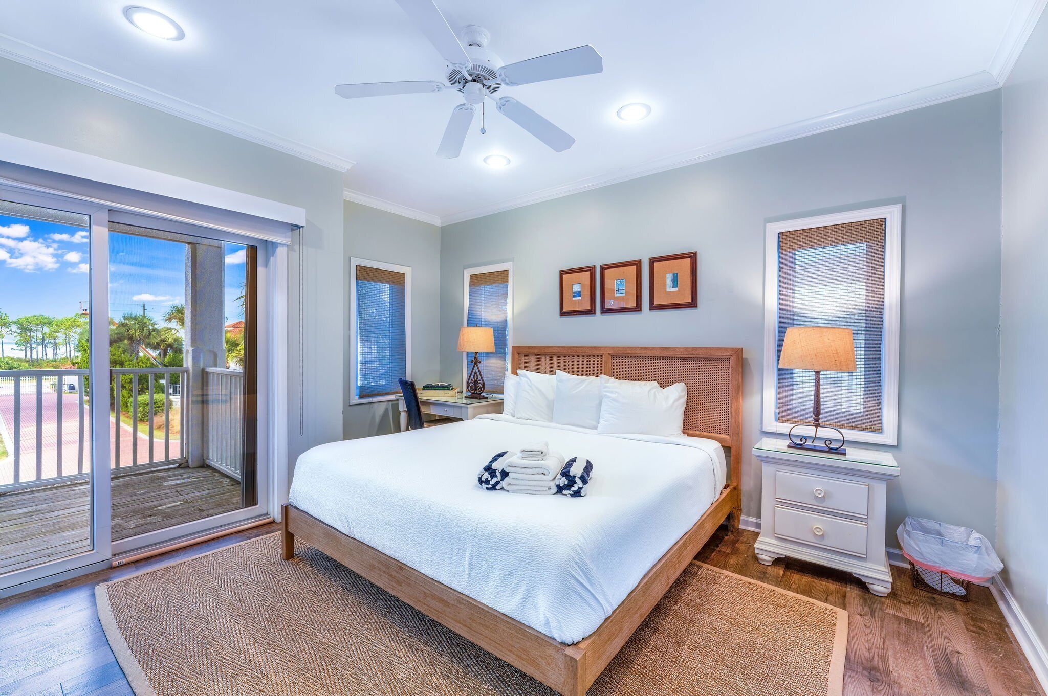 A bedroom with a large bed, a ceiling fan, a nightstand, a lamp, and a view of the outdoors.