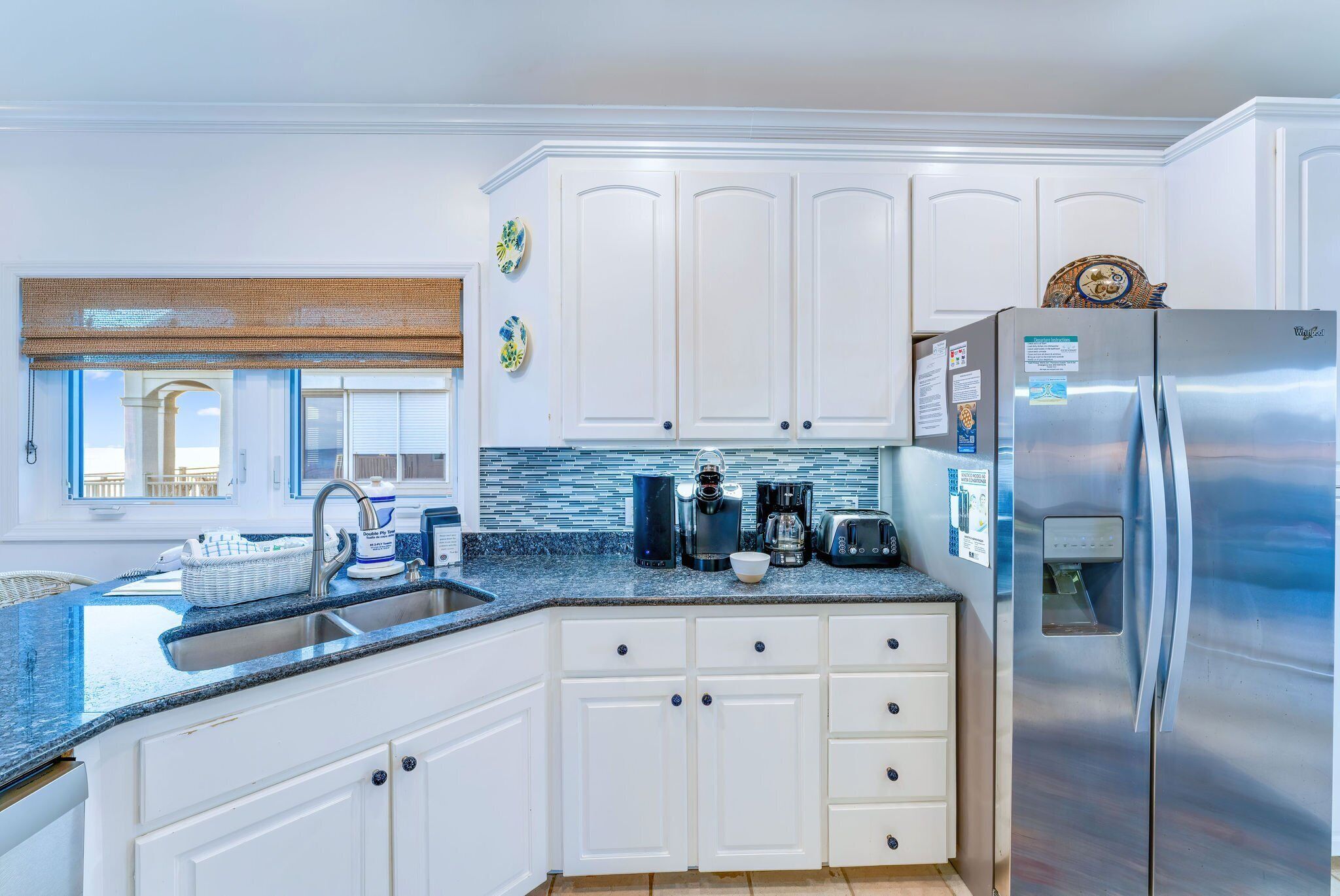 Una cocina moderna con armarios blancos, un refrigerador de acero inoxidable y una encimera de granito.