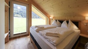 Camera da letto in una baita di legno con un letto grande, una finestra e vista su un prato.
