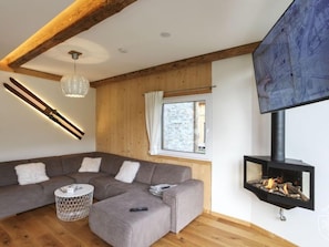 Una sala de estar moderna con un sofá modular, una chimenea, un televisor y un techo de madera.