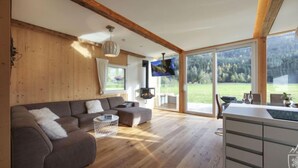 Un ampio soggiorno con soffitto in legno, un divano spazioso, un tavolo da pranzo e una TV a parete.