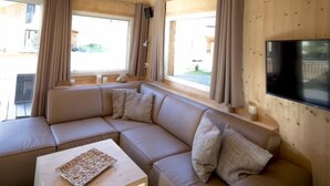 A modern cabin interior with a sectional sofa, a small wooden table, and a flat-screen TV mounted on the wall.