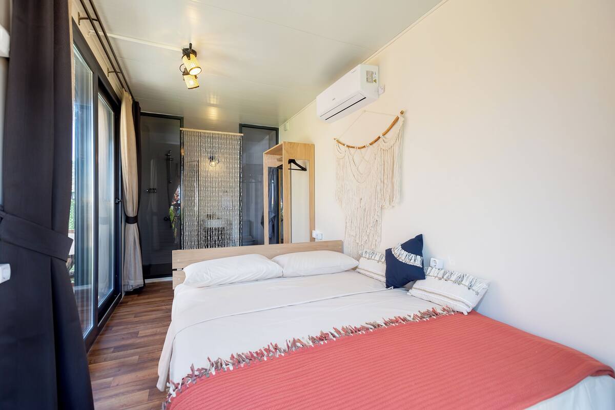 Ett modernt hotellrum med en stor säng, en garderob, en spegel och en väggdekoration i form av en hängande makramé.