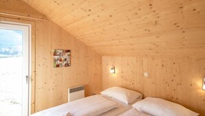 Habitación de cabaña de madera con dos camas, una ventana y una lámpara fijada a la pared.