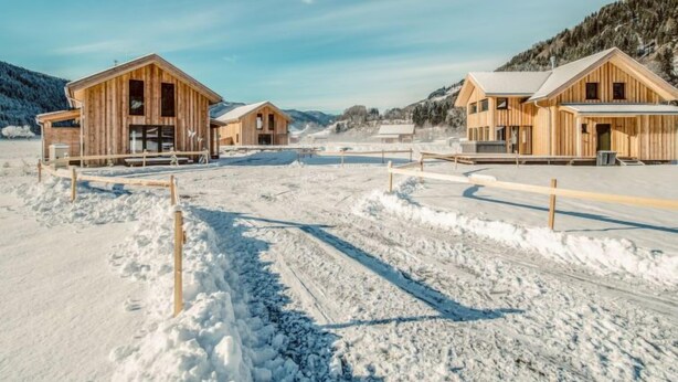 Paisaje nevado con cabañas de madera y cielo despejado.