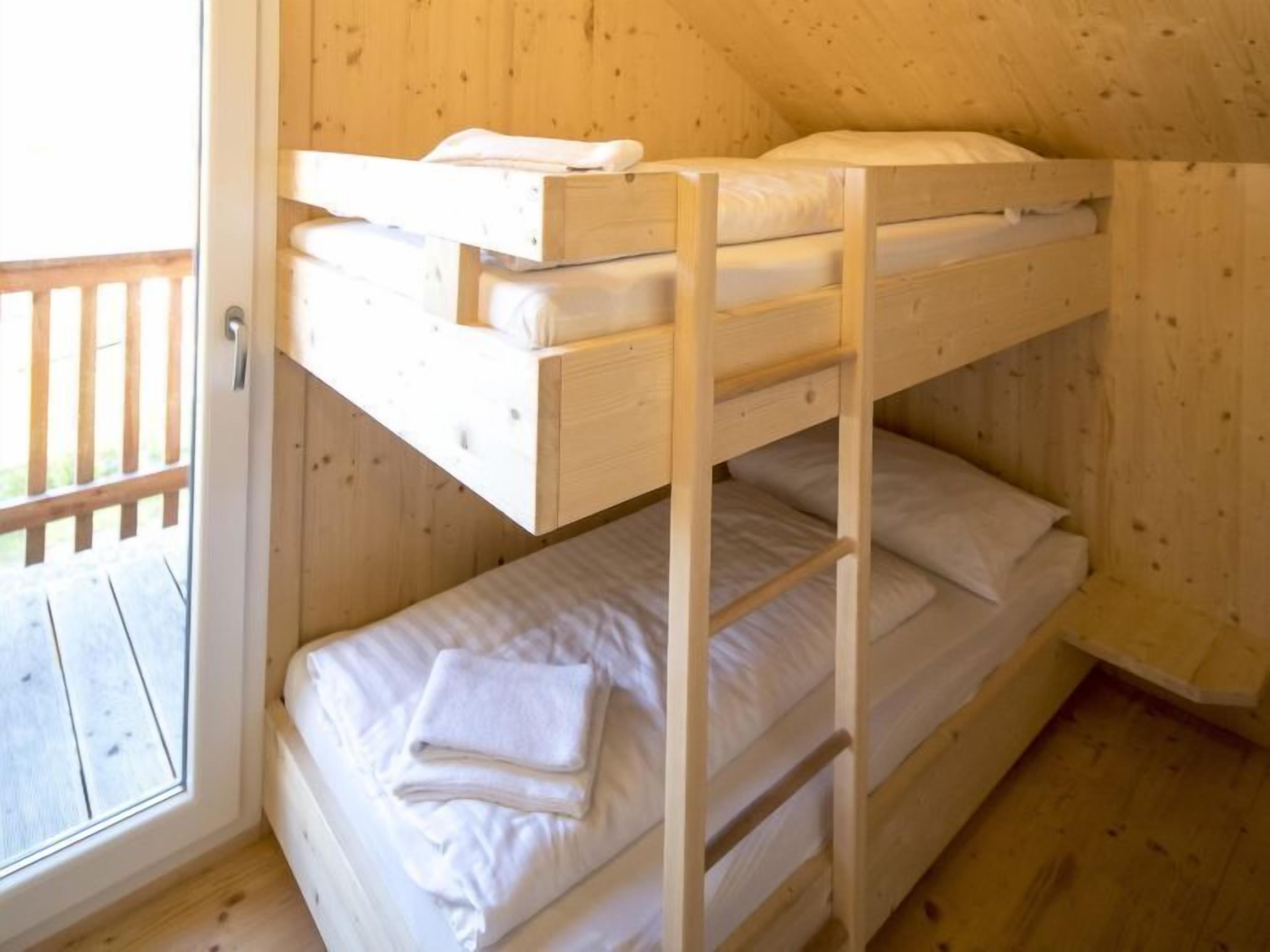 A bunk bed room with wooden walls and a wooden deck outside.