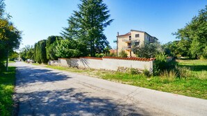 Una strada residenziale con una casa a due piani, una strada asfaltata e vegetazione circostante.