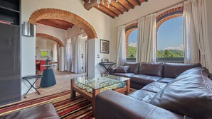 Un salón espacioso con sofá de cuero, una mesa de centro de vidrio y vistas a un paisaje exuberante a través de ventanales arqueados.