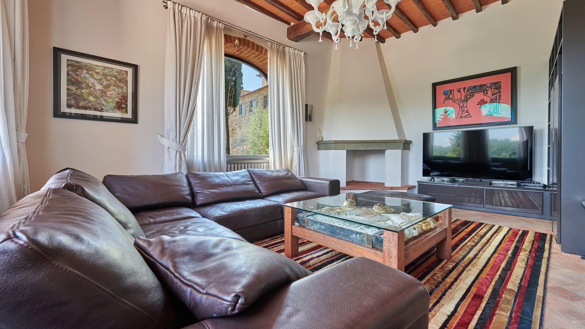 A modern living room with a leather sectional sofa, a glass coffee table, a flat-screen TV, and a large window with curtains.