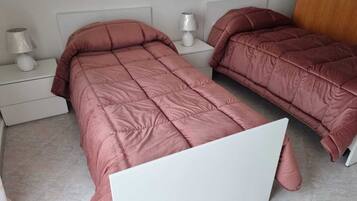 Une chambre avec deux lits, deux tables de chevet blanches et une porte.