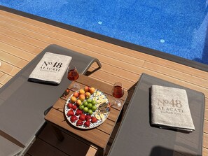 A poolside table with a plate of fruit, two glasses of red wine, and a towel with "No 18 Alacati Boutique Hotel" printed on it. - No 48 Alaçatı (Cesme)