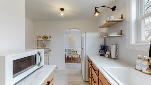 A modern kitchen with white cabinetry, a built-in oven, a coffee maker, and a view into the dining area.