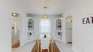 A dining area with a white table, chairs, and a chandelier. There are white cabinets with glass doors and a sign that says "EAT" on the wall.