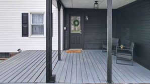 A covered porch with a dark door, a doormat, and a bench.