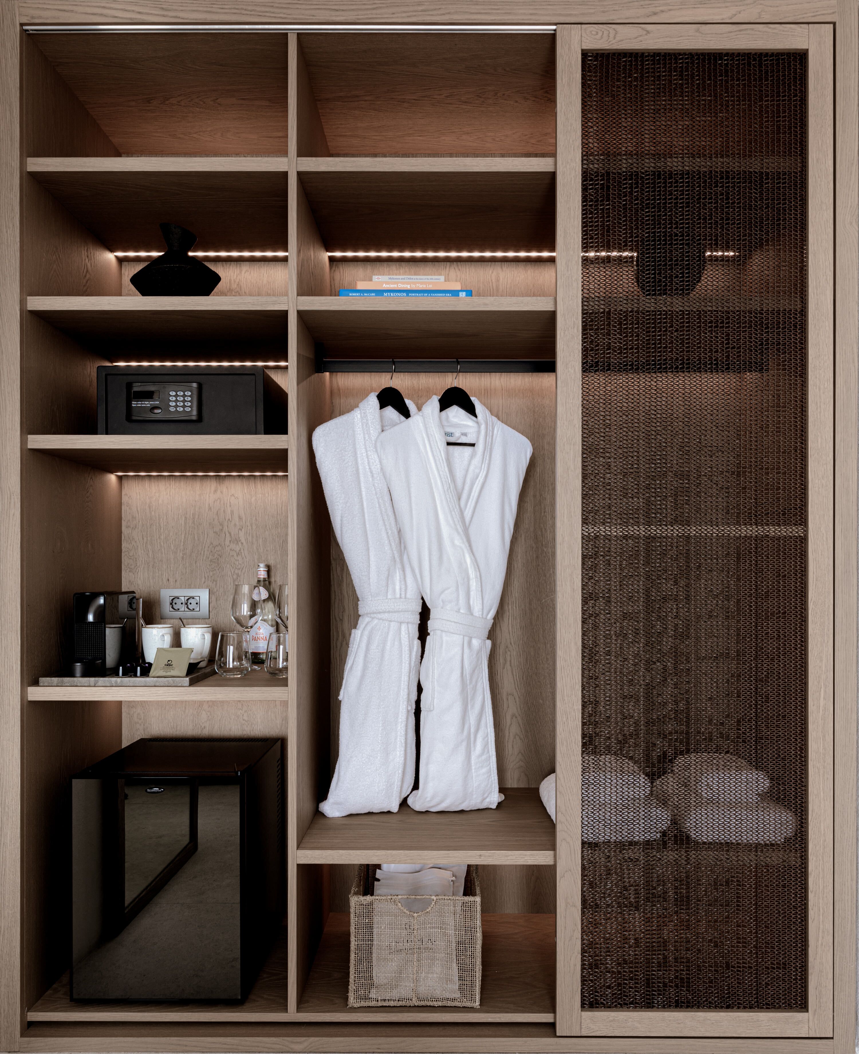 A wooden wardrobe with a mesh screen door, a black radio, a coffee machine, and two white bathrobes hanging.