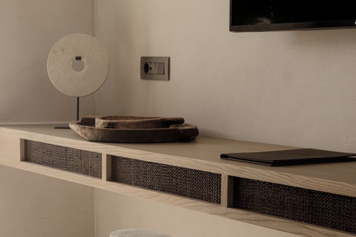 Een moderne, minimalistisch ingerichte kamer met een ingebouwd bureau, een ronde tafel en een comfortabele zithoek.