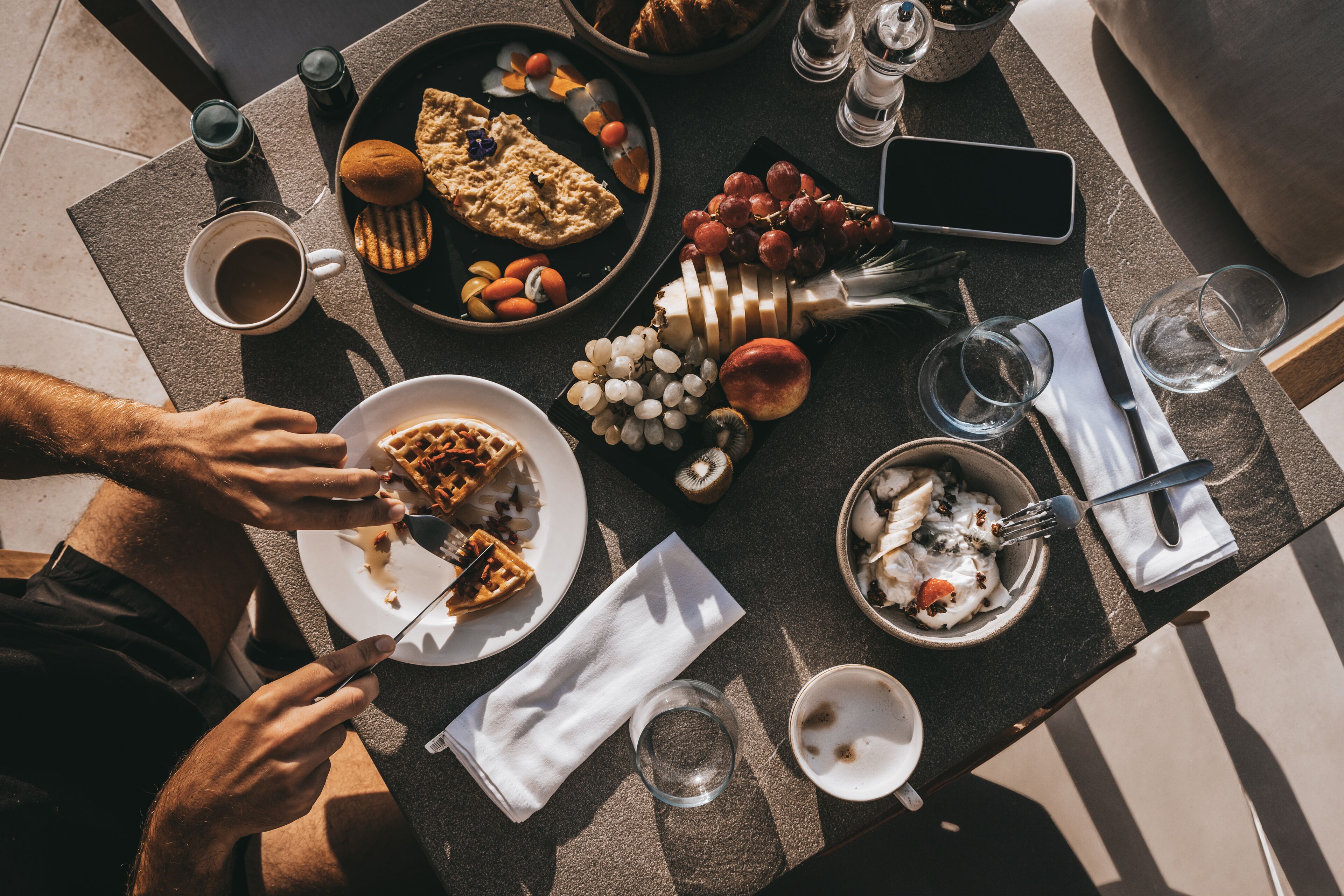 A dining table with various food items, utensils, and a smartphone.
