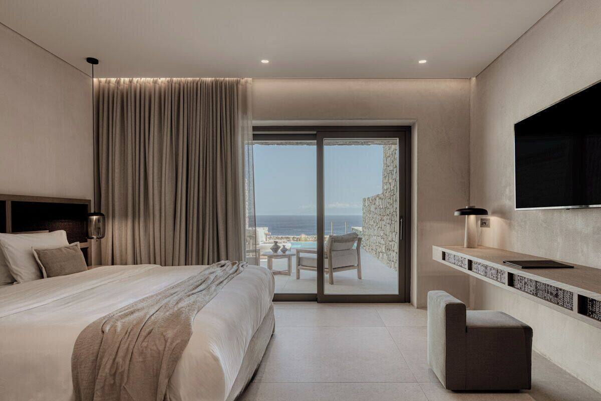 Ein modernes Hotelzimmer mit einem großen Bett, einem Flachbildfernseher, einem Balkon mit Blick auf den Pool und einer Schiebetür nach draußen.