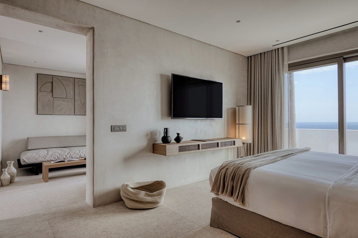 Una camera d'albergo moderna con un letto grande, una TV a parete, un comodino, una lampada da comodino e vista sul mare.
