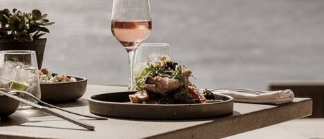 A table set with a meal, a glass of wine, and a view of the ocean.