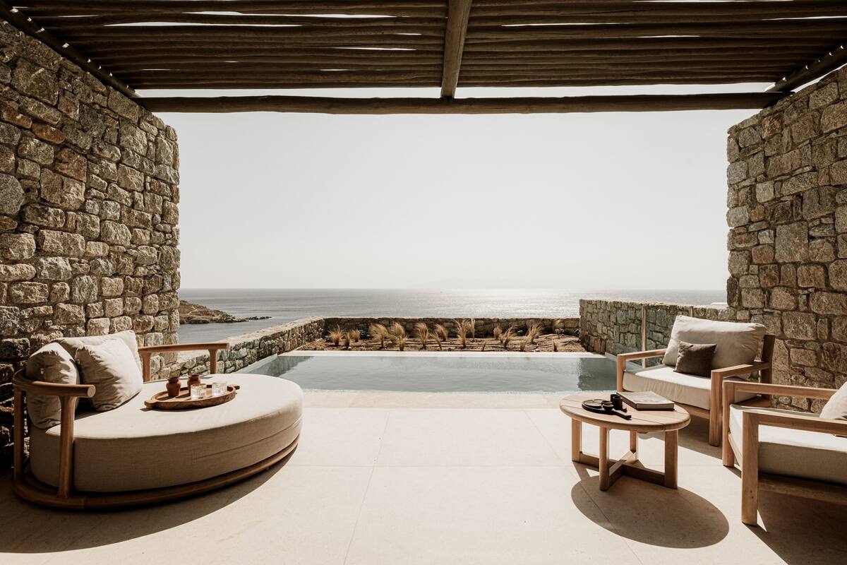 Ein Endlospool mit Steinwänden und Meerblick, umgeben von Holzmöbeln und einer Pergola.