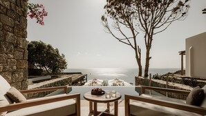 Une terrasse offrant une vue sur la mer, avec une table en bois, deux canapés et un mur en pierre.
