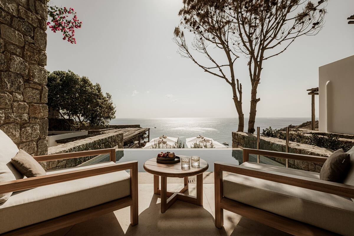 Eine Terrasse mit Meerblick, ausgestattet mit einem Holztisch, zwei Sofas und einer Steinmauer.