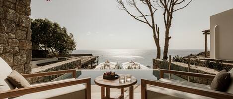 A terrace with a view of the sea, featuring a wooden table, two sofas, and a stone wall.