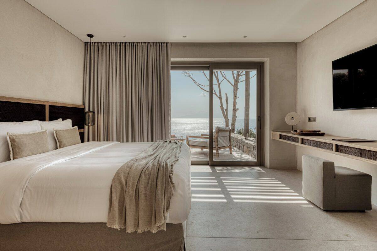 Ein modernes Hotelzimmer mit einem großen Bett, einem Fernseher, einem Schreibtisch und Blick auf das Meer.