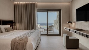 Une chambre d’hôtel moderne dotée d’un grand lit, d’un coin salon avec vue sur la mer et d’un téléviseur à écran plat fixé au mur.
