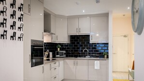 A modern kitchen with white cabinets, a black backsplash, and a microwave. - Designer 2-bed 2-bath apartment with a garden (London)