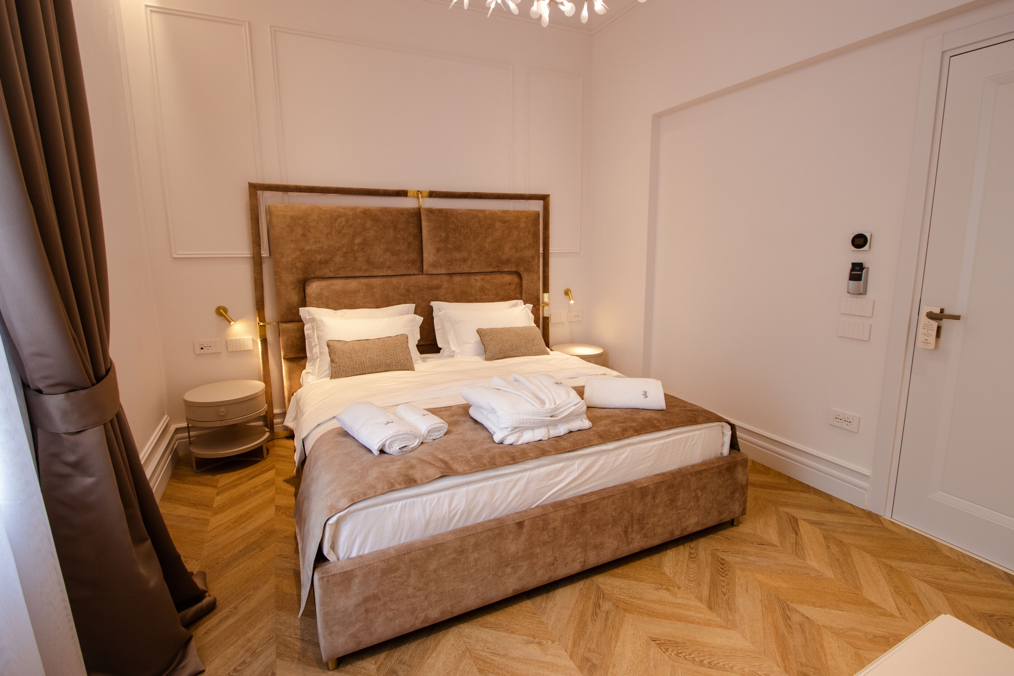 A neatly made bed with a headboard, a bedside table with a lamp, and a door with a lock.