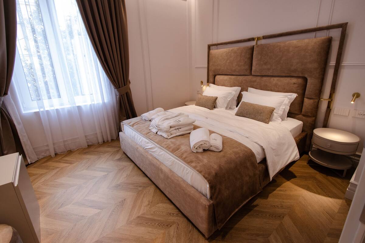 Una cama bien hecha con ropa de cama blanca y marrón, un cabecero de madera y una mesita de noche con una lámpara.