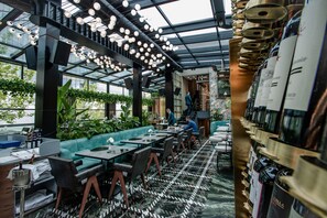 A modern restaurant with a long counter, green seating, and a variety of wine bottles on display. - The Crown Boutique Hotel & SPA (Tirana)