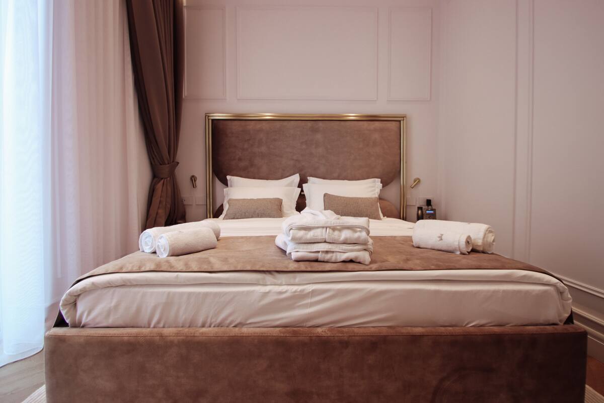 Una cama bien hecha con un cabecero grande, almohadas y toallas dobladas.