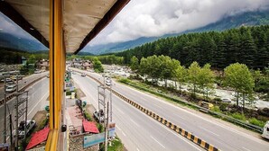A road with a bridge overhead, surrounded by greenery and mountains. - Hotel Beas regency (Manali)