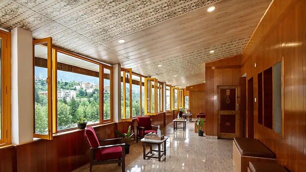 A hotel lobby with wooden walls, large windows, and a marble floor. - Hotel Beas regency (Manali)
