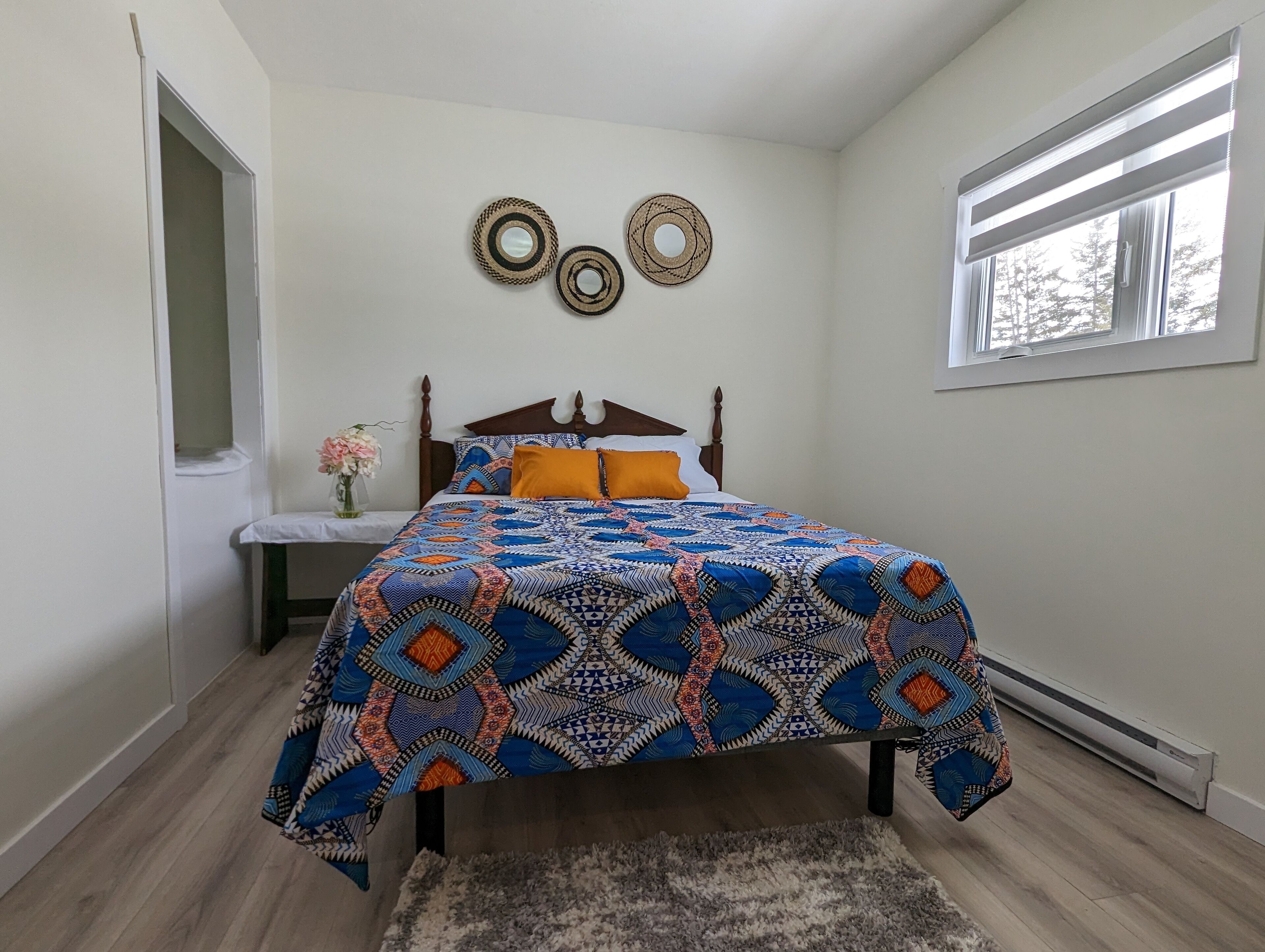 Een slaapkamer met een houten bed, een bed met een patroon, twee decoratieve elementen aan de muur, een raam en een deur.