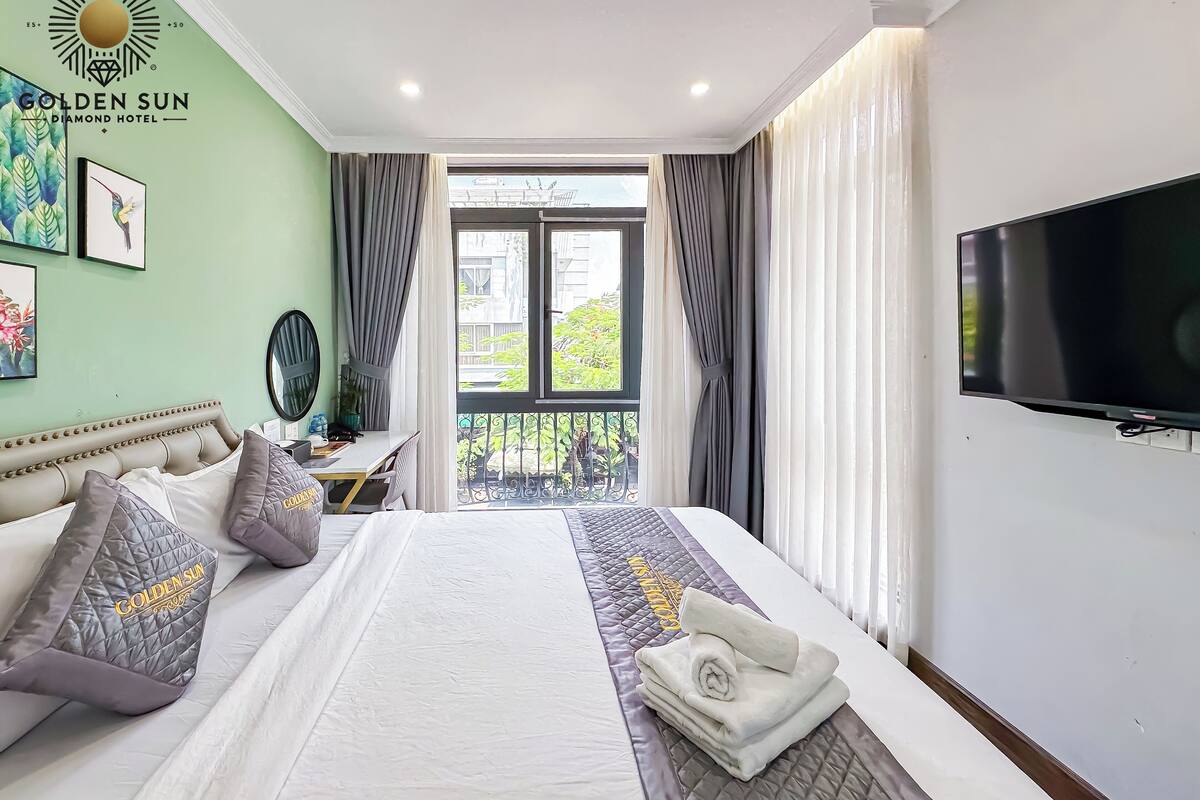 A hotel room with a bed, a desk, a TV, and a balcony with a view.