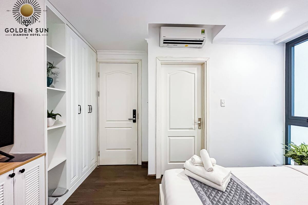 A hotel room with a bed, a wardrobe, a TV, and an air conditioning unit.