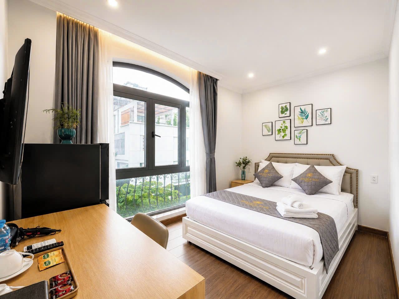 Una habitación de hotel con una cama, un escritorio, un televisor y un ventanal con cortinas.