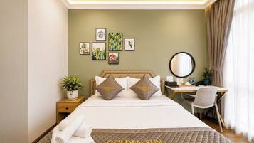 A hotel room with a bed, a desk, and a chair. There are pillows with the hotel's name on them.